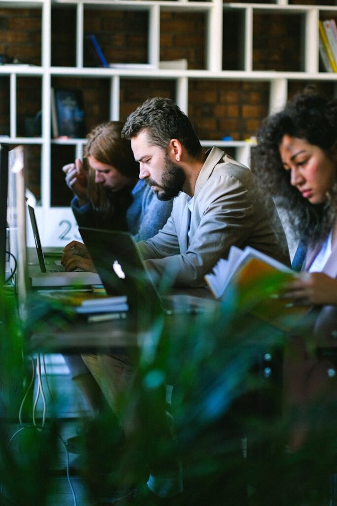 Thoughtful young colleagues in formal clothes sitting at desk with books and browsing netbooks while working in modern business center